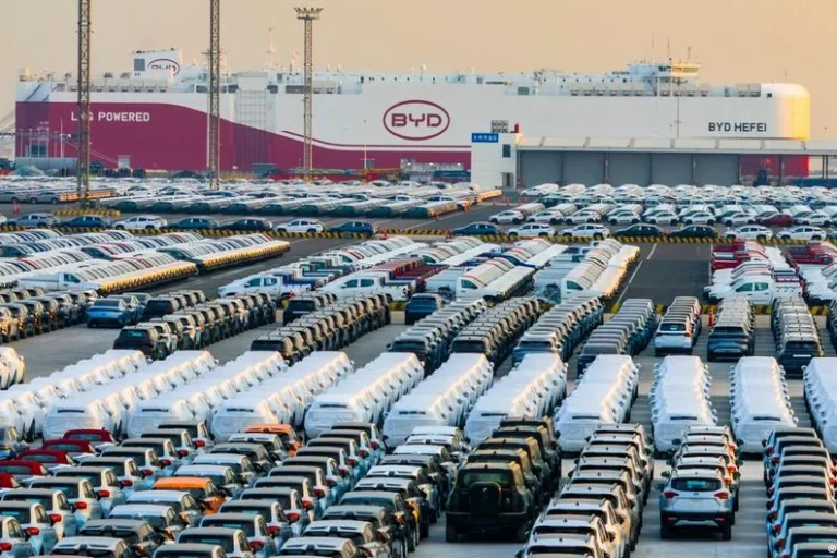 Extensive car storage lot at a BYD facility, rows of parked cars with a BYD building in the background