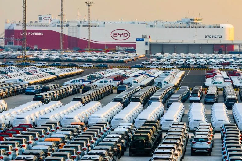 Extensive car storage lot at a BYD facility, rows of parked cars with a BYD building in the background